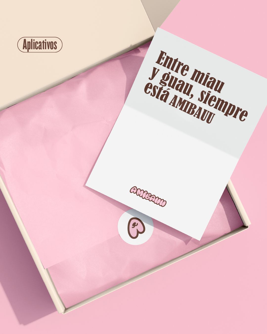 Caja abierta con papel de seda rosa y una tarjeta que dice Entre miau y guau, siempre está AMIBAUU